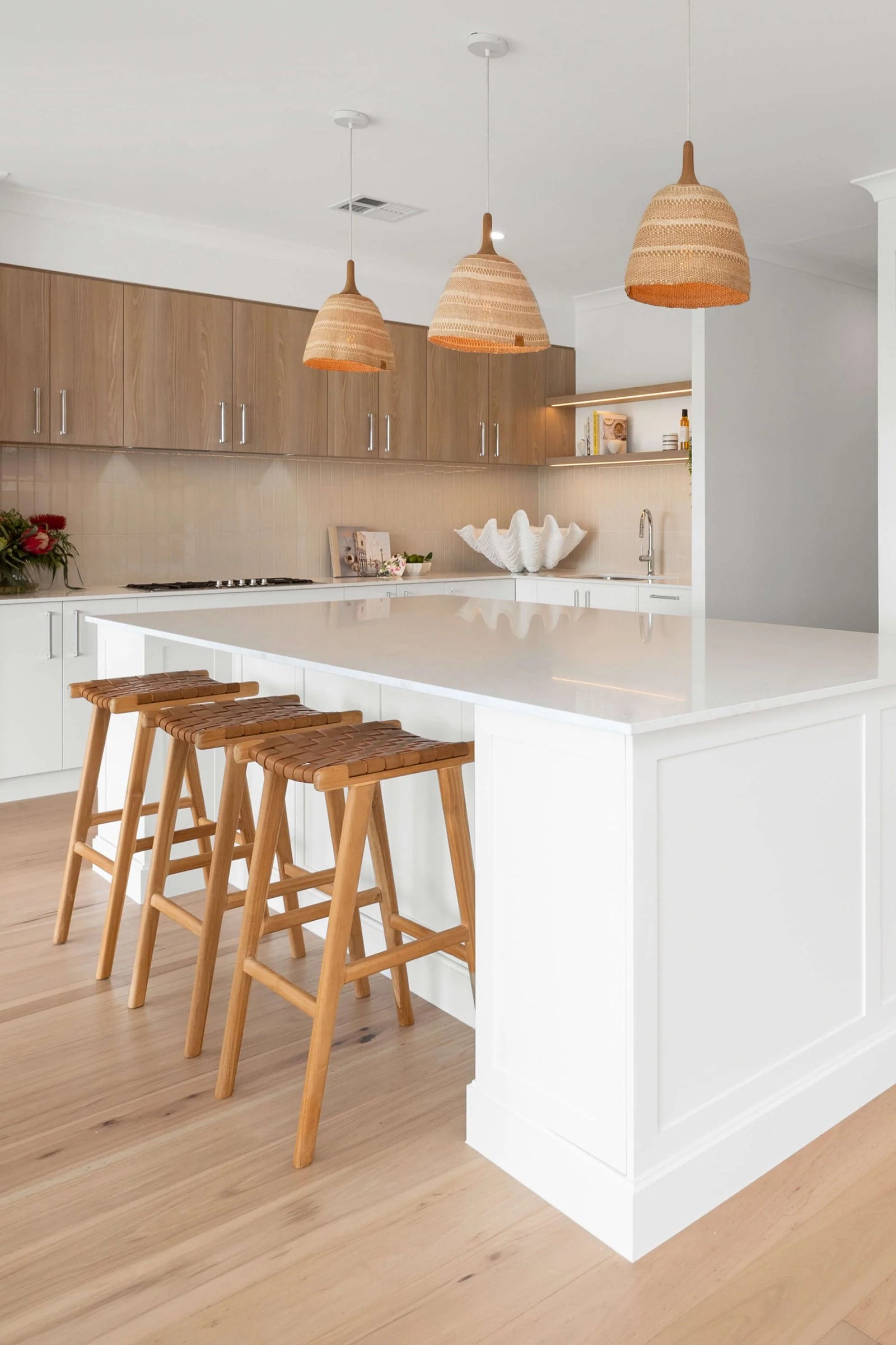 Modern kitchen with white island, wooden stools, and pendant lights.