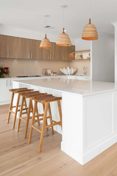 Modern kitchen with white island, wooden stools, and pendant lights.